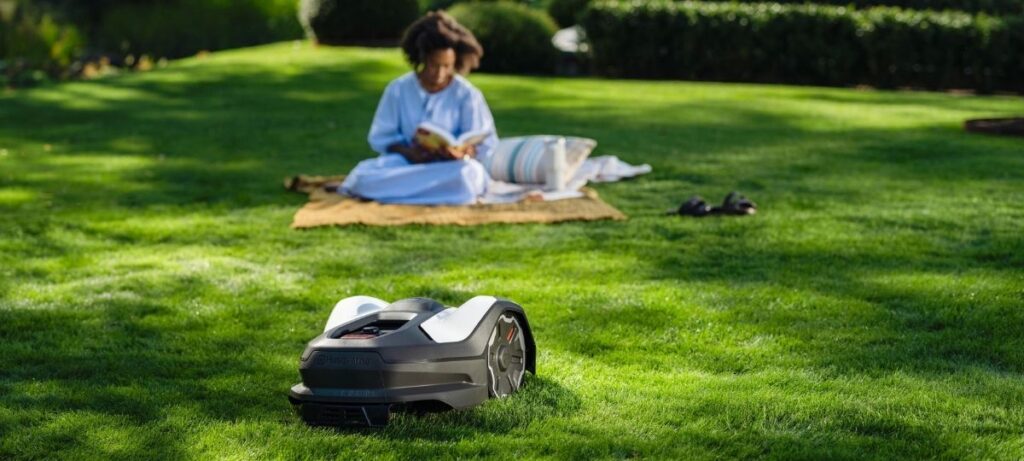 Husqvarna Automower NERA robotic mower cutting lawn while person relaxes in garden