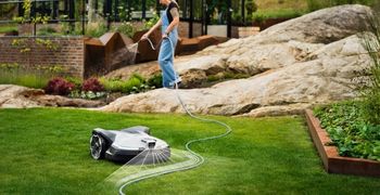 Robotic lawn mower maintaining a neatly striped lawn in a landscaped garden.