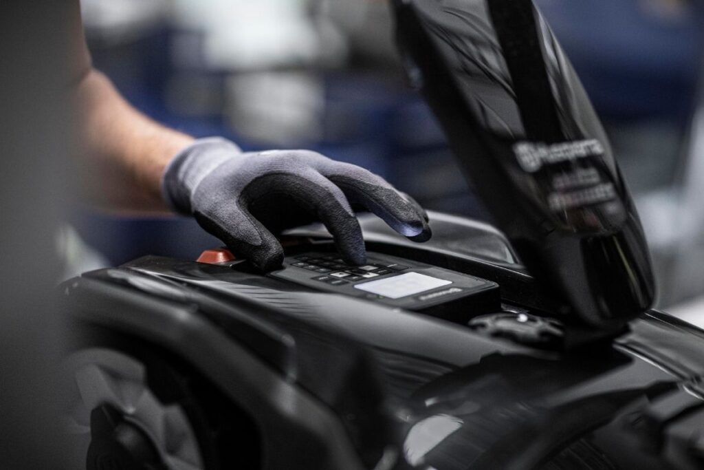 Technician servicing garden machinery while wearing protective gloves.